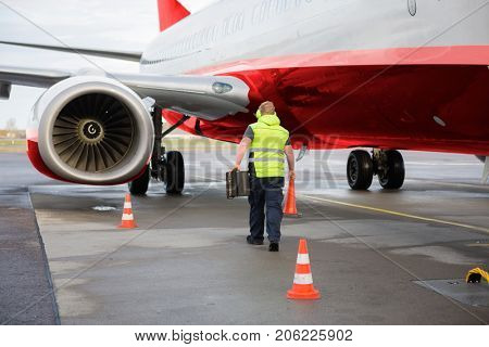 Worker Carrying Traffic Cone And Chocks By Airplane On Runway