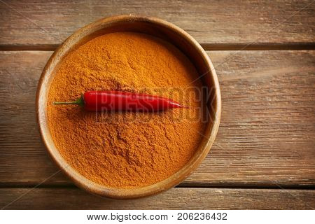 Chili powder and raw pepper in bowl on wooden background