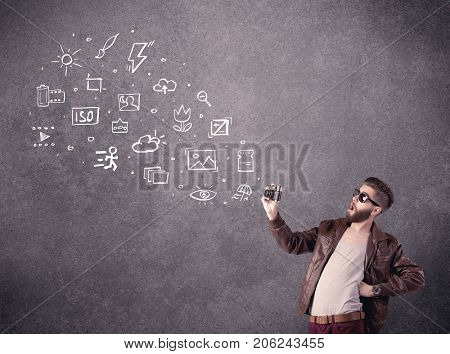 An elegant hipster guy trying to use a vintage camera with camera settings icons drawn on wall, like flash, white balace or ISO value concept
