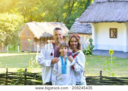 Ukrainian family in traditional clothing vyshyvanka with embroidery over landscape of tipical ucrainian village, summer outdoor. Slavic mother, father and son, noise added.