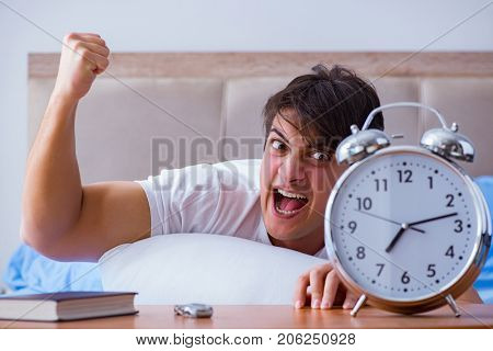 Man in bed frustrated suffering from insomnia with an alarm cloc