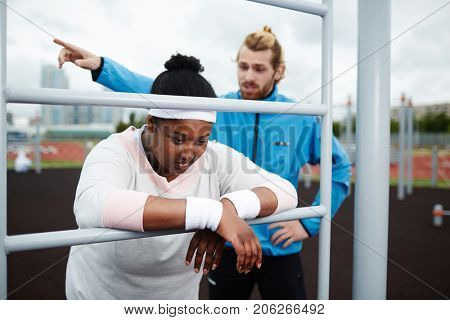 Young trainer making plus-sized woman work harder and motivating her to continue exercising