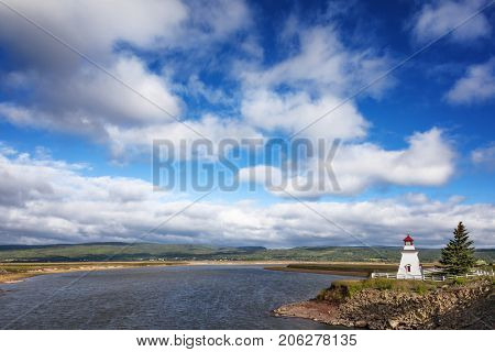 Anderson Hollow lighthouse by the Shepody River dam in Harvey, Bay of Fundy, New Brunswick. Beautiful summer day with calm water and blue sky cloudsape. 