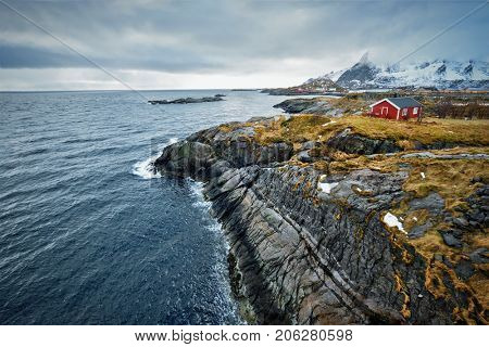 Clif with traditional red rorbu house on Litl-Toppoya islet on Lofoten Islands, Norway in winter