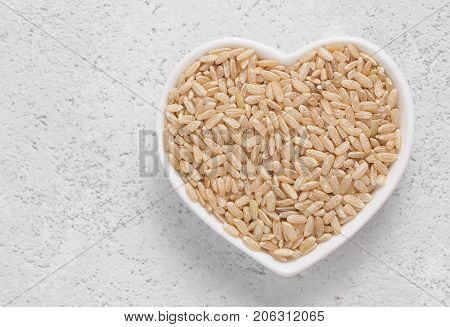 Brown rice in heart-shaped bowl on gray cement background. Top view or flat lay.