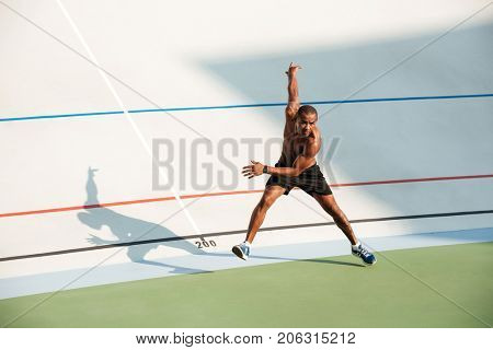 Full length portrait of a half naked muscular sportsman starting to run on a track field outdoors