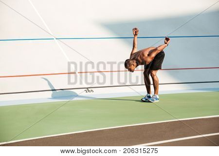 Full length portrait of a half naked strong fit african sportsman jumping at the track field outdoors