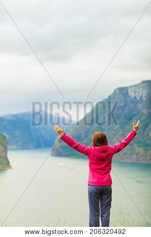 Travel concept. Happy free tourist woman in happiness and elated enjoyment with arms raised outstretched up looking at fjords mountains in Norway