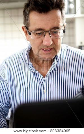 Senior man working on laptop computer at home.