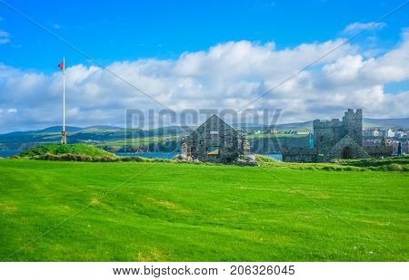 The remains of Peel Castle constructed by vikings on top of Peel hill with Isle of Man national flag on a clear blue sky
