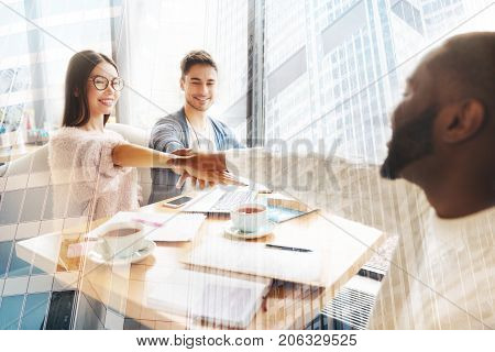 Best team. Happy enthusiastic colleagues putting hands together while sitting at the table and having adorable time together