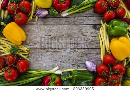 Frame from fresh and ripe vegetables on wooden background. Healthy vegetarian food with space for text.