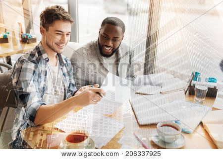 Studying with pleasure. Close up of cheerful pleasant students spending free time on studying while sitting at the table and expressing concern