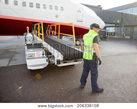 Worker Standing By Luggage Conveyor Attached To Airplane