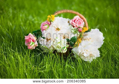 Basket full of flowers roses peony camomile on the grass.