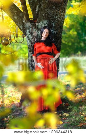young mother waiting for the child's birth with a pensive and tender look tenderly keeps rakum a tummy happy pregnancy against the background of greens in the park the gentle loving relations