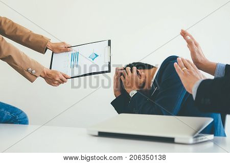 Angry boss giving a document to a sad employee sitting in a desk at office