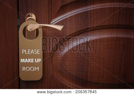 Closed door with sign PLEASE MAKE UP ROOM on handle at hotel