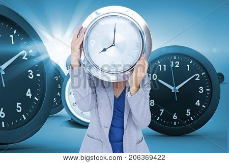 Businesswoman holding clock in front of face against digital composite image of clocks