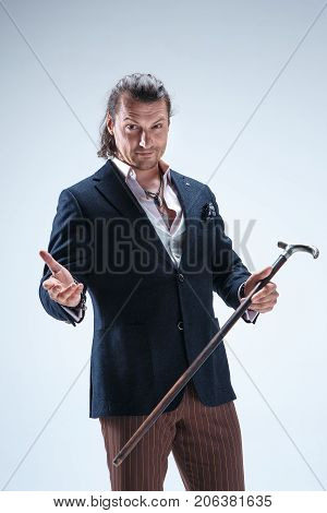 The mature bearded man in a suit holding cane. Isolated on a blue studio background.