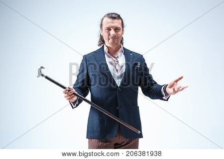 The mature bearded man in a suit holding cane. Isolated on a blue studio background.