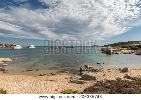 Two catamaran sailing yachts moored off the coast of Cavallo island near Corsica with sandy beach and rocks in the foreground turquoise Mediterranen and blue sky above