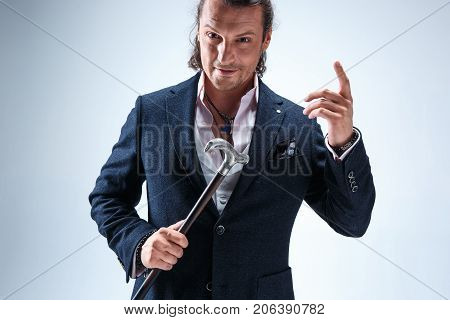 The mature bearded man in a suit holding cane. Isolated on a blue studio background.