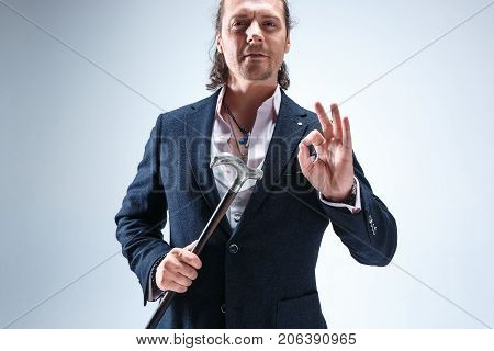 The mature bearded man in a suit holding cane. Isolated on a blue studio background.
