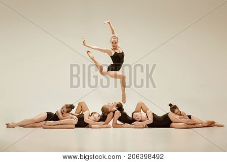 The group of modern ballet dancers dancing on gray studio background
