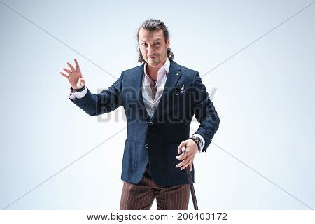 The mature bearded man in a suit holding cane. Isolated on a blue studio background.