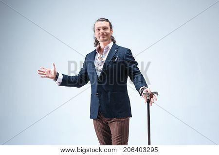 The mature bearded man in a suit holding cane. Isolated on a blue studio background.