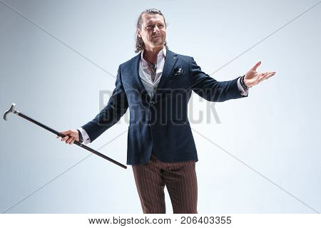 The mature bearded man in a suit holding cane. Isolated on a blue studio background.