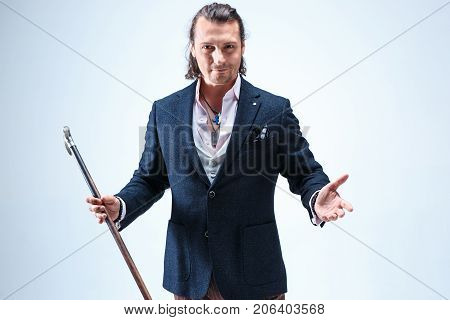 The mature bearded man in a suit holding cane. Isolated on a blue studio background.