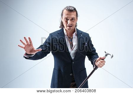 The mature bearded man in a suit holding cane. Isolated on a blue studio background.