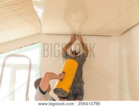 Workers stretch the stretch ceiling in the room .