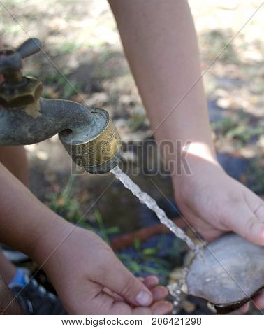 Girl cleaning an empty shell from a lake mussel with an outdoor running faucet.
