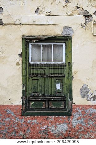 green old shabby window in a decaying house with weathered wood and peeling paint set in a yellow flaking concrete wall