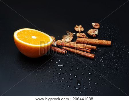Walnuts, delicious fresh orange and cinnamon sticks are depicted on dark gray background. Copy space. Close-up of objects.