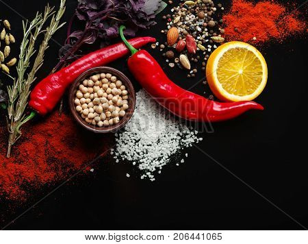 Two red pods of chili pepper, a slice of fresh orange, various fragrant species on a black background. Close-up of vegetables. Copy space.