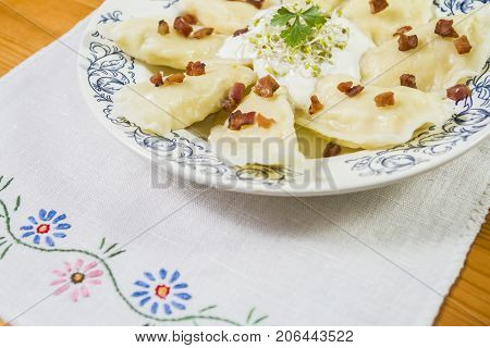 Cooked dumplings with cheese pork scratching and creme fraiche on wooden table. Polish ukrainian russian traditional food.