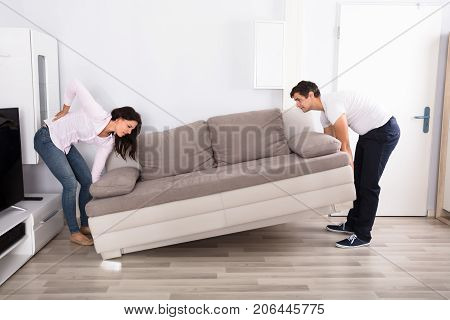 Young Woman Having Backpain While Lifting The Sofa With Her Husband