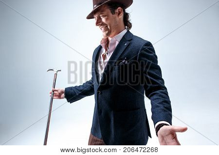 The mature bearded man in a suit and hat holding cane. Isolated on a gray studio background.