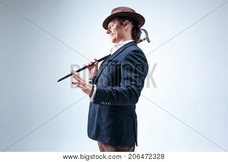 The mature bearded man in a suit and hat holding cane. Isolated on a gray studio background.