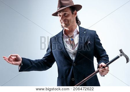 The mature bearded man in a suit and hat holding cane. Isolated on a gray studio background.