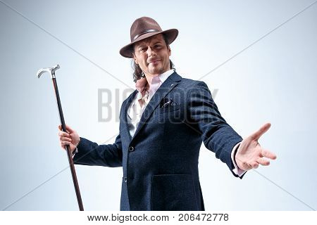 The mature bearded man in a suit and hat holding cane. Isolated on a gray studio background.