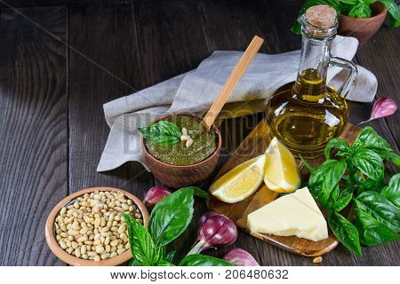 Tradizione Italiana Homemade Pesto recipe ingredients on dark table. Parmesan cheese, basil leaves, pine nuts, olive oil, garlic.