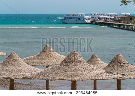 A view of the red sea in Egypt with wicker peaks from umbrellas in the foreground.