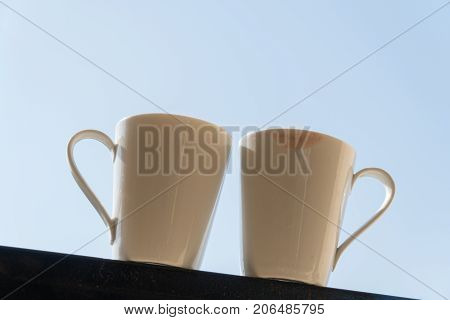 Two white mugs stand on the balcony in the background of the sky. On one mug there are traces of female lips.