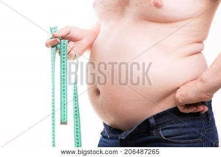 Overweight man with fat folds holding green centimeter tape in his hand closeup isolated on white background. Obesity concept