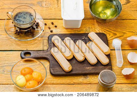 Picture of ingredients for dessert, Savoyardi cookies on cutting board, coffee, cream cheese, yolks, proteins